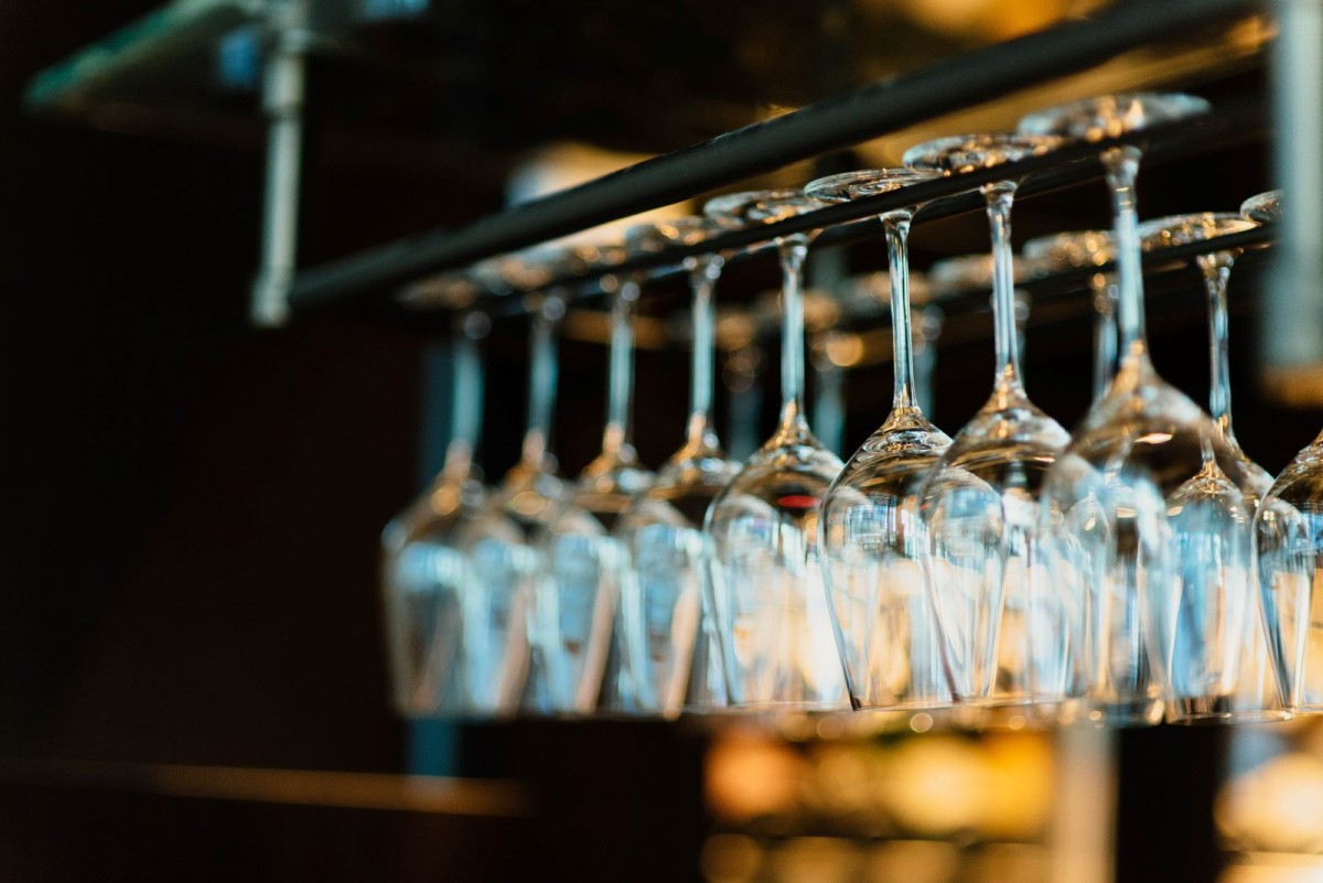 Two rows of wine glasses hang above a bar